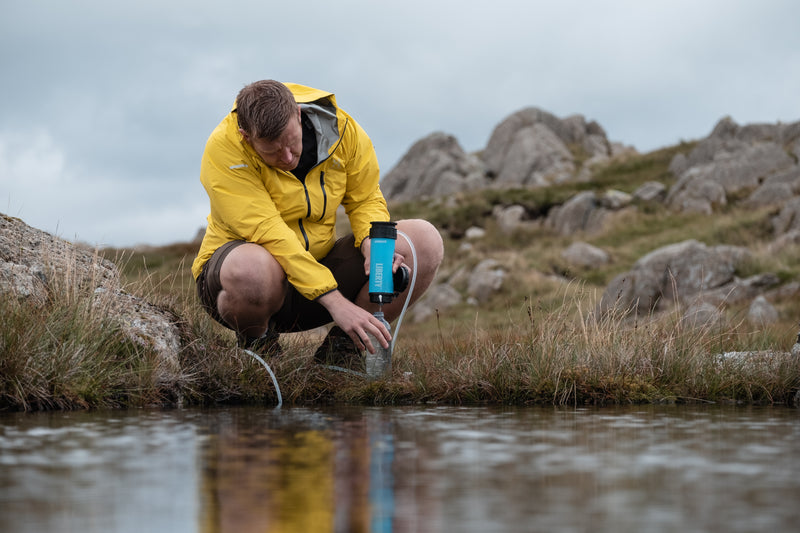Laden Sie das Bild in Galerie -Viewer, A man purifying lake water using a LifeSaver Liberty bottle